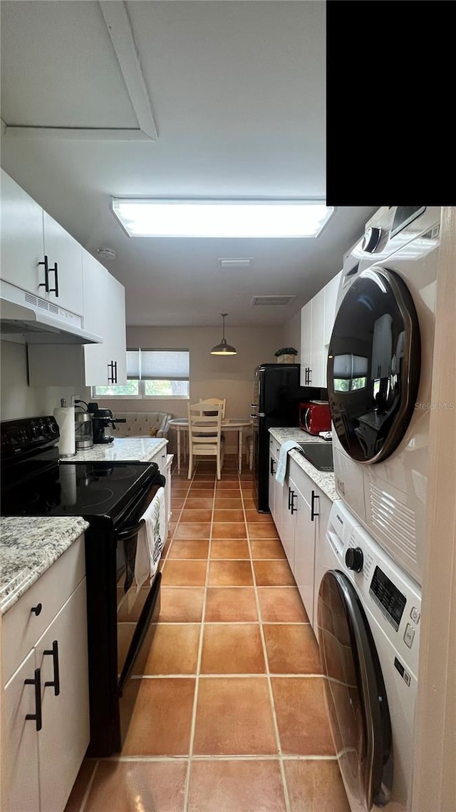 kitchen with light tile patterned floors, black appliances, stacked washing maching and dryer, white cabinets, and light stone countertops