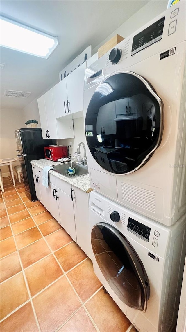 laundry area with light tile patterned flooring, stacked washer and dryer, and sink