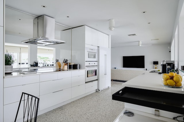 kitchen featuring modern cabinets, light speckled floor, island exhaust hood, and visible vents