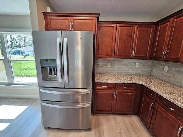 kitchen featuring light wood-style floors, light stone counters, stainless steel fridge with ice dispenser, and tasteful backsplash