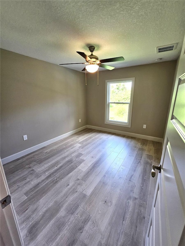 empty room featuring visible vents, a ceiling fan, a textured ceiling, wood finished floors, and baseboards