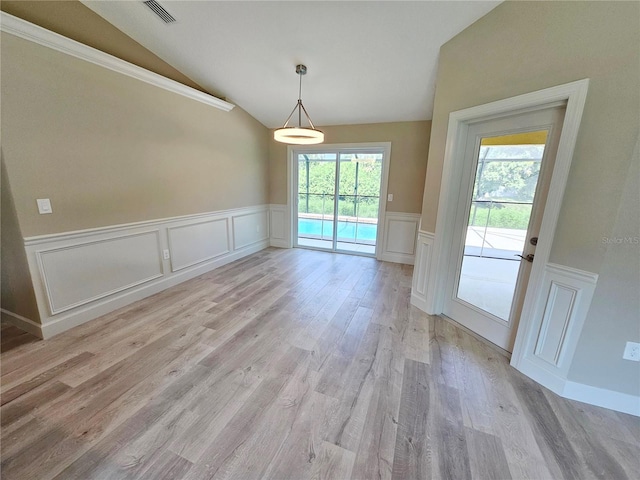 unfurnished dining area with vaulted ceiling, light wood-style flooring, wainscoting, and visible vents