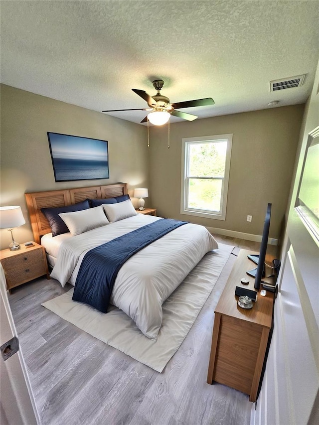 bedroom featuring baseboards, visible vents, ceiling fan, wood finished floors, and a textured ceiling