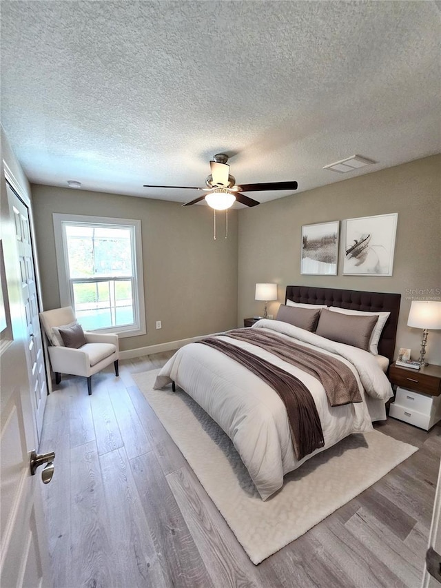 bedroom featuring ceiling fan, a textured ceiling, visible vents, and wood finished floors