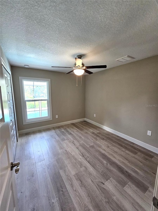 empty room featuring a textured ceiling, wood finished floors, visible vents, and baseboards