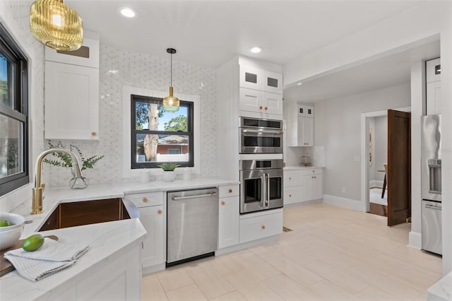 kitchen featuring sink, hanging light fixtures, stainless steel appliances, light stone countertops, and white cabinets