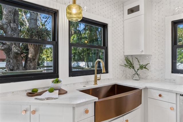 kitchen with white cabinetry, sink, light stone countertops, and hanging light fixtures