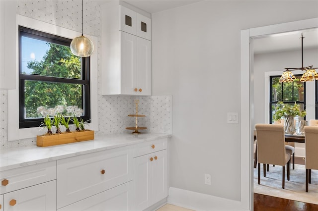 kitchen with light stone counters, tasteful backsplash, hanging light fixtures, and white cabinets