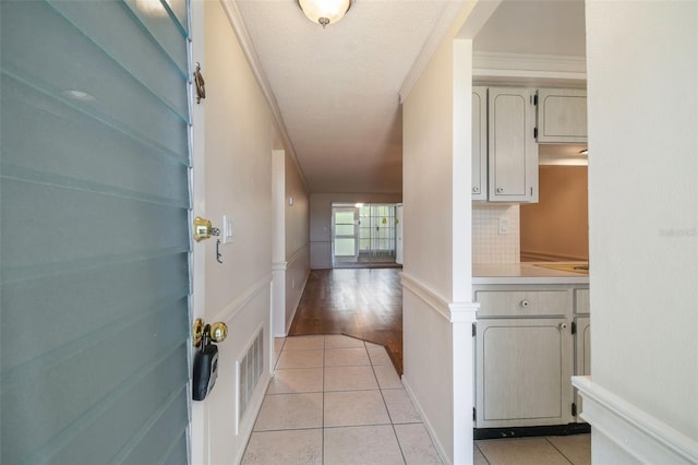 hall with crown molding, a textured ceiling, and light tile patterned floors