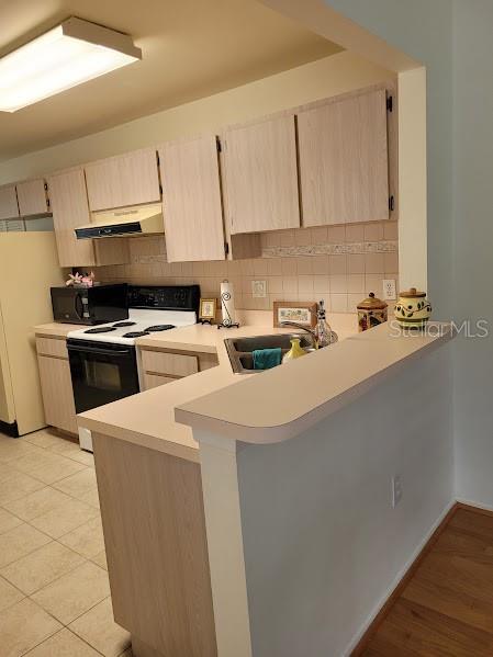 kitchen featuring white appliances, sink, light tile patterned floors, light brown cabinetry, and kitchen peninsula