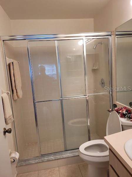 bathroom featuring tile patterned flooring, vanity, toilet, and a shower with shower door