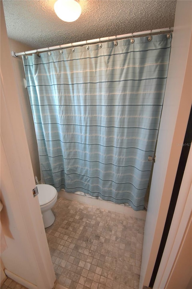 bathroom featuring toilet, a textured ceiling, and a shower with curtain