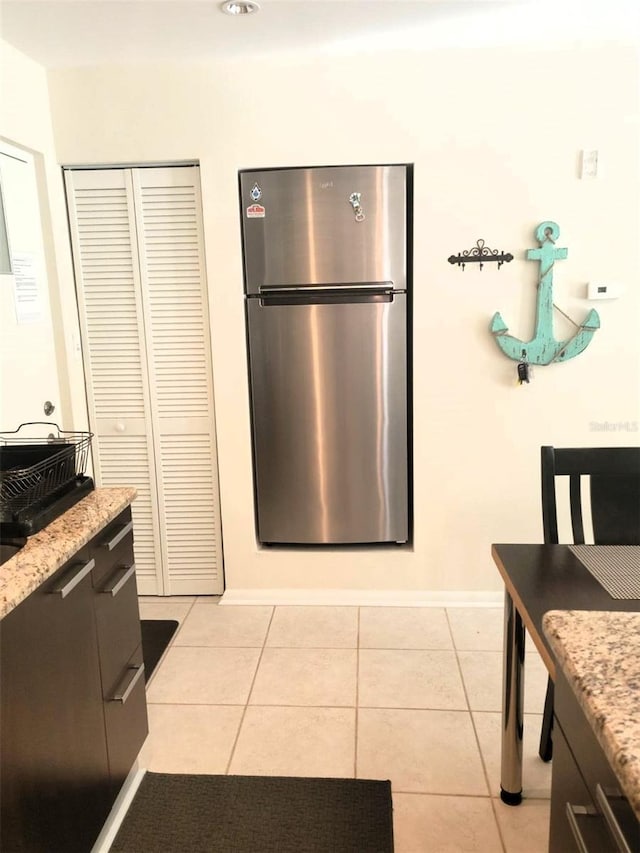 kitchen with light tile patterned flooring, light stone countertops, and stainless steel refrigerator