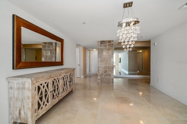 hallway with light tile patterned floors, ornate columns, and a chandelier