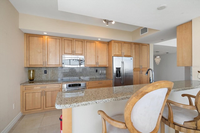 kitchen featuring a breakfast bar area, stainless steel appliances, a peninsula, visible vents, and light stone countertops