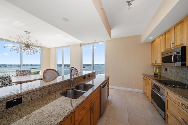 kitchen featuring light stone counters, a water view, a sink, appliances with stainless steel finishes, and backsplash