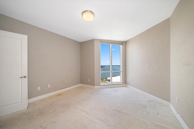 empty room with a water view, baseboards, and light colored carpet