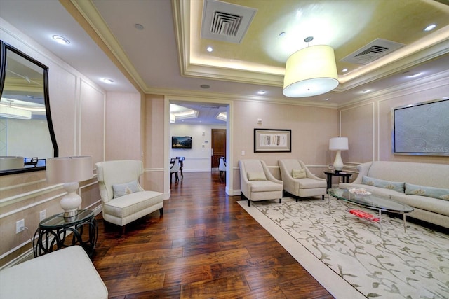 living room featuring a tray ceiling, dark wood-style flooring, visible vents, and a decorative wall