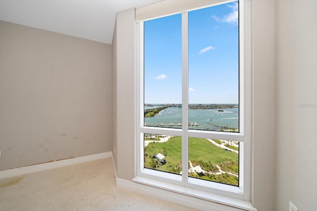 interior space featuring light colored carpet, a water view, plenty of natural light, and baseboards