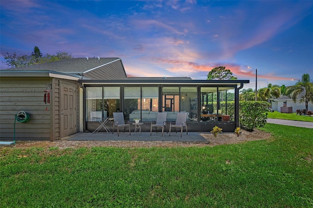 back house at dusk featuring a yard, a patio, and a sunroom