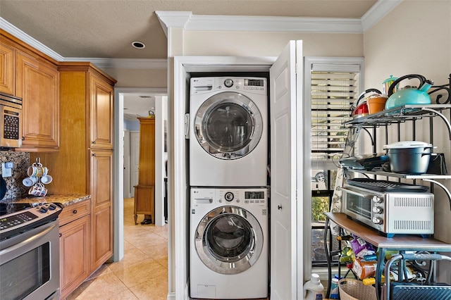 clothes washing area with a textured ceiling, light tile patterned floors, crown molding, and stacked washer and clothes dryer