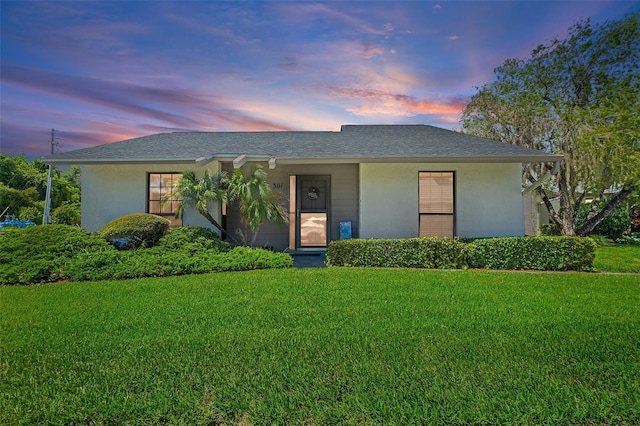 ranch-style home with a yard, roof with shingles, and stucco siding