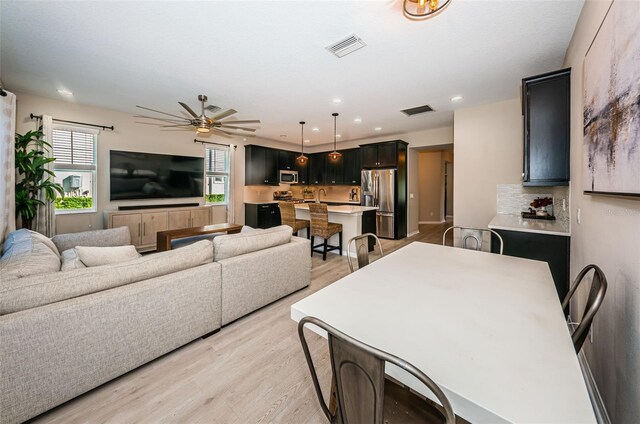 kitchen with ceiling fan, stainless steel appliances, tasteful backsplash, light hardwood / wood-style flooring, and pendant lighting