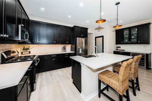 kitchen featuring wine cooler, a kitchen island with sink, sink, and appliances with stainless steel finishes