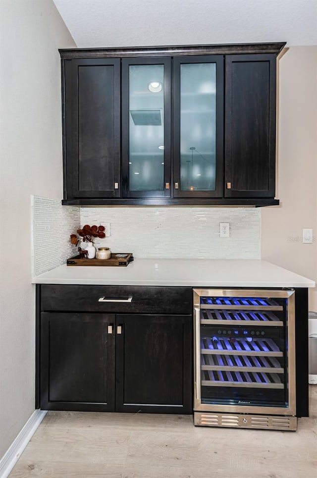 bar with backsplash, beverage cooler, and light wood-type flooring