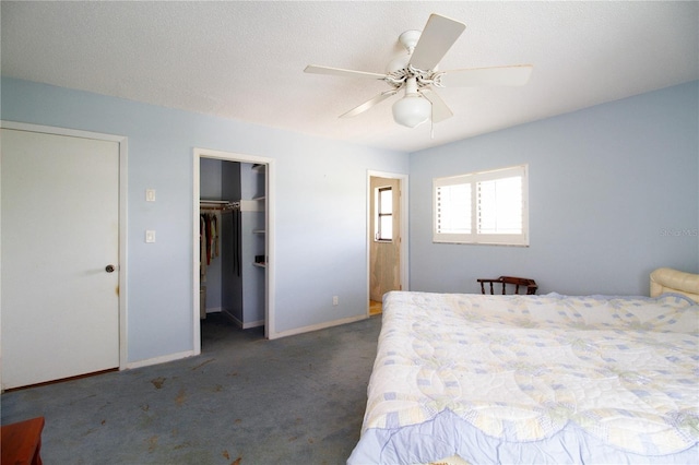 unfurnished bedroom with ceiling fan, dark colored carpet, a textured ceiling, a spacious closet, and a closet