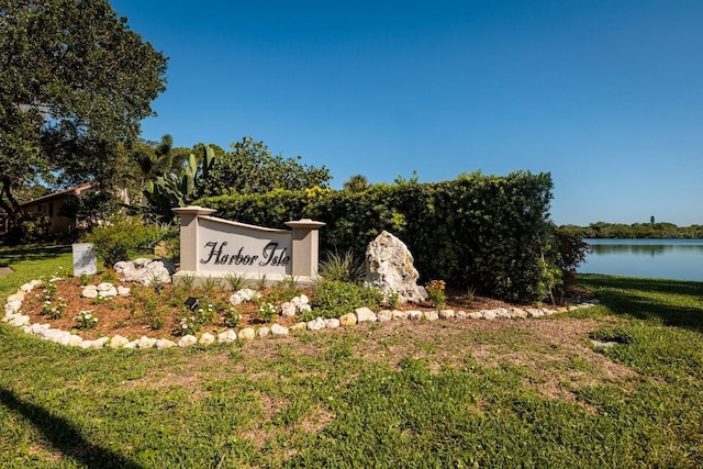 community / neighborhood sign featuring a lawn and a water view