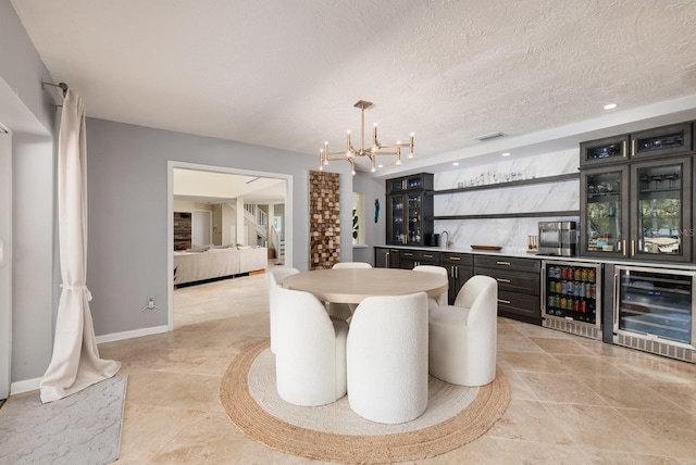 dining area featuring a notable chandelier, a textured ceiling, wine cooler, and bar area