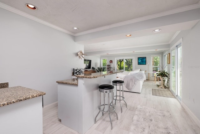 kitchen with a kitchen breakfast bar, light hardwood / wood-style floors, light stone counters, and crown molding