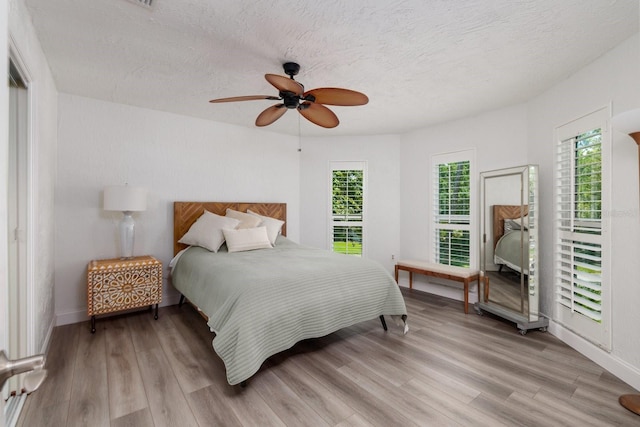 bedroom with ceiling fan, light wood-type flooring, and a textured ceiling