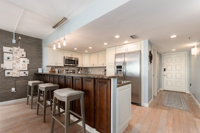 kitchen with stainless steel appliances, kitchen peninsula, dark stone countertops, a breakfast bar, and white cabinets