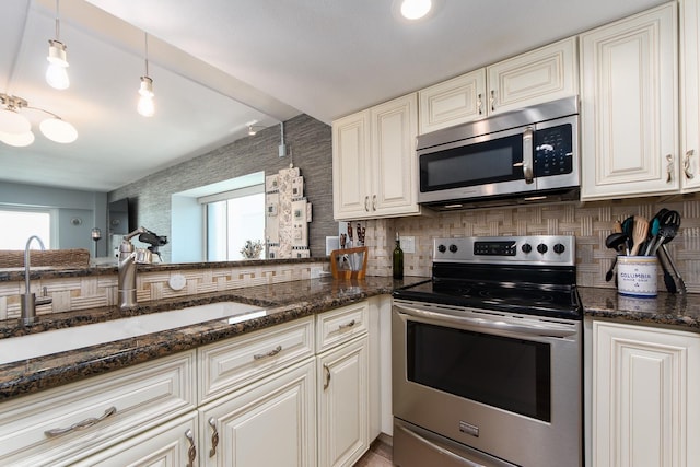 kitchen with sink, hanging light fixtures, backsplash, dark stone countertops, and appliances with stainless steel finishes