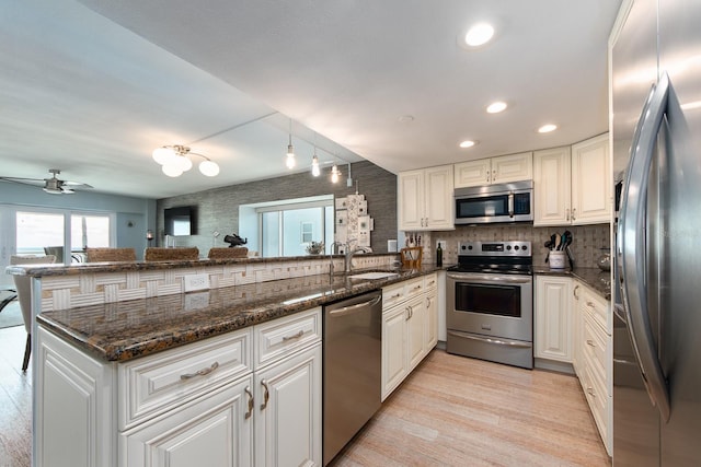 kitchen featuring kitchen peninsula, dark stone countertops, white cabinets, and appliances with stainless steel finishes