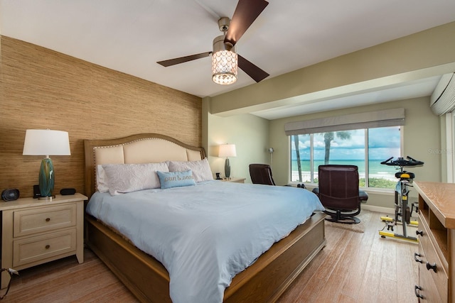 bedroom featuring ceiling fan, an AC wall unit, and light hardwood / wood-style flooring