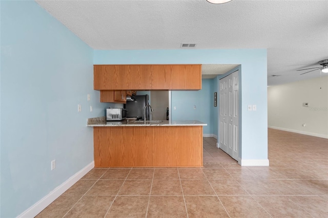 kitchen with ceiling fan, light tile patterned floors, kitchen peninsula, and a textured ceiling