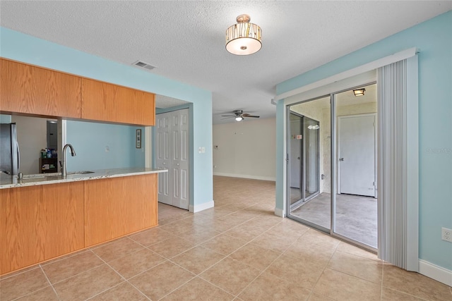 kitchen with sink, ceiling fan, light stone counters, a textured ceiling, and kitchen peninsula