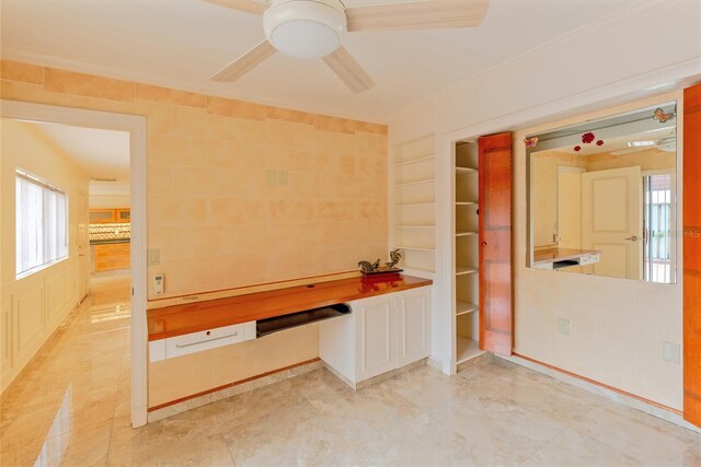 unfurnished office featuring built in shelves, ceiling fan, and light tile patterned floors