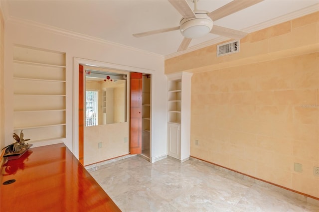 tiled empty room with built in shelves, ornamental molding, and ceiling fan