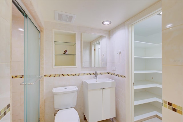 bathroom featuring tile walls, a shower with shower door, toilet, and vanity