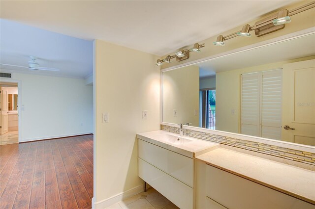 bathroom with backsplash, vanity, ceiling fan, wood-type flooring, and ornamental molding