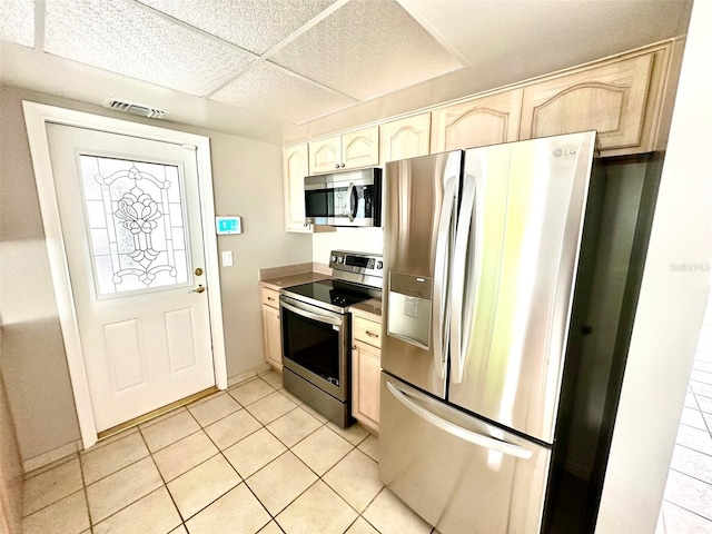 kitchen with a drop ceiling, light tile patterned floors, light brown cabinets, and appliances with stainless steel finishes