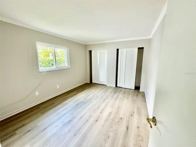 unfurnished bedroom with crown molding, light wood-type flooring, and two closets