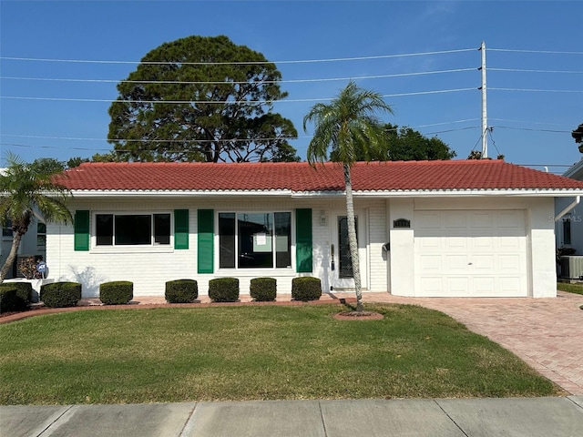 view of front facade with central air condition unit, an attached garage, a tile roof, a front yard, and decorative driveway