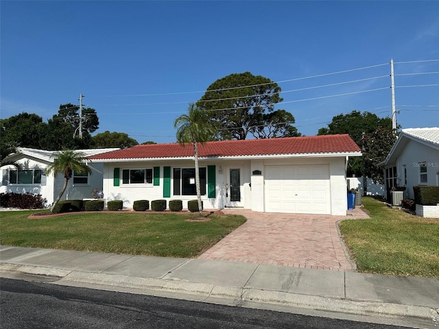 ranch-style house featuring a tile roof, an attached garage, a front lawn, and decorative driveway