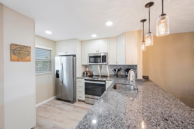 kitchen with appliances with stainless steel finishes, stone counters, sink, pendant lighting, and light wood-type flooring