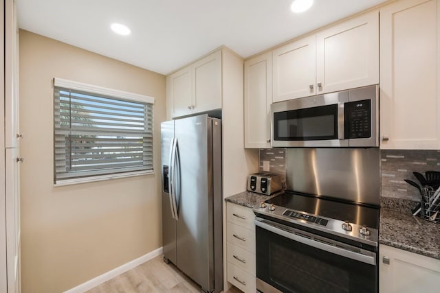 kitchen featuring stainless steel appliances, backsplash, light hardwood / wood-style flooring, and dark stone countertops